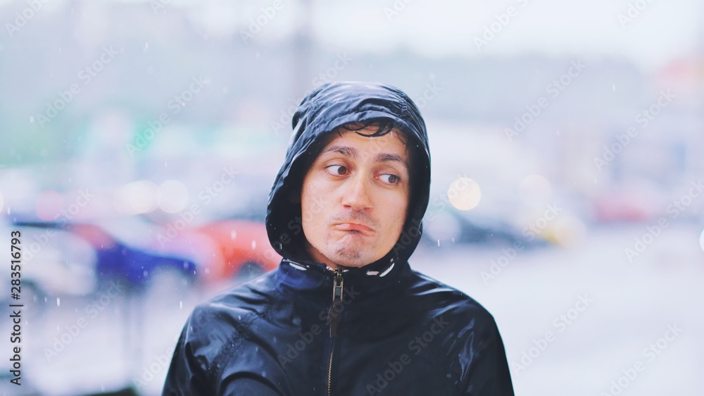 Portrait of a sad man in a raincoat and a hood in the rain. Bad stormy rainy weather concept. Portrait of a sad man in a raincoat and a hood in the rain. Bad stormy rainy weather concept.