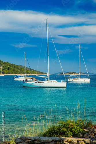 Scenic view of Kosirina beach bay on Murter island in Croatia, anchored sailing boats and yachts on blue sea, view through the pines