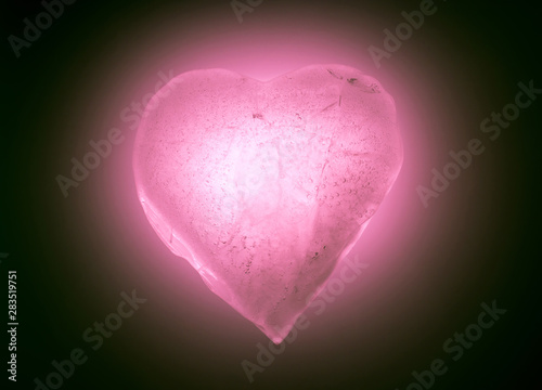 Ice frozen heart symbol of soft pink color close-up glowing in the dark. Texture of ice with bubbles.