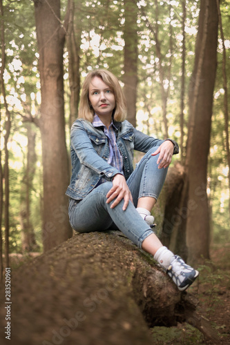 young beautiful caucasian woman, blonde, in jeans clothes, in a forest in autumn at sunset