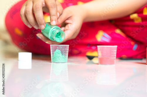Young girl putting in mica color colourant into transparent measuring cups for making homemade hand made soap