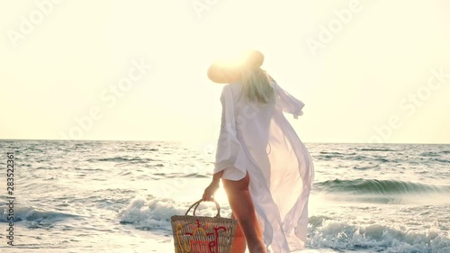 Gorgeous blonde woman 20s in summer straw hat walking outdoors on the beach photo