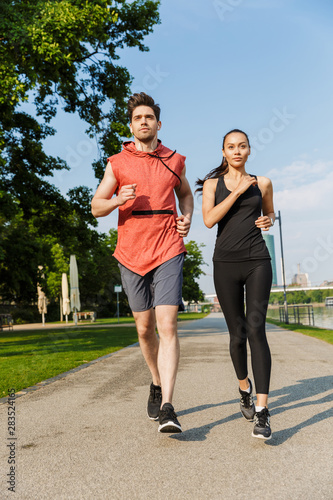Photo of athletic focused man and woman doing workout and running on city riverfront © Drobot Dean