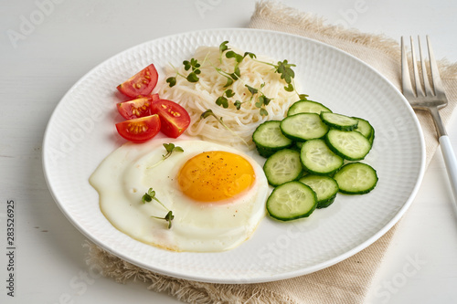 Healthy breakfast - fried egg with cherry tomatoes and cucumber on light white background, fodmap dash diet, gluten free, side view closeup