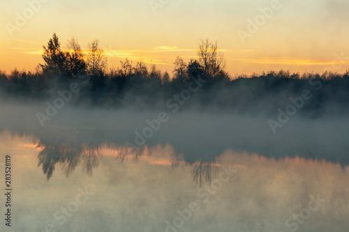 forest lake with fog over the water at dawn of an autumn day