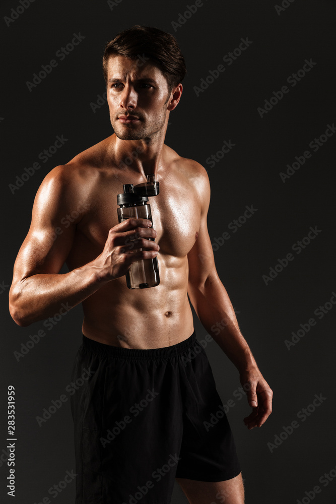 Concentrated handsome young strong sportsman posing isolated over black wall background bottle with water.
