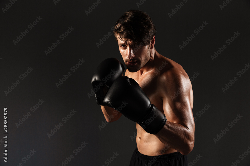 Handsome young strong sportsman boxer in gloves make exercises boxing isolated over black wall background.