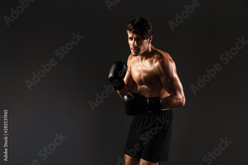 Handsome young strong sportsman boxer in gloves make exercises boxing isolated over black wall background.