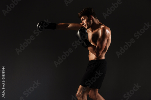 Handsome young strong sportsman boxer in gloves make exercises boxing isolated over black wall background.