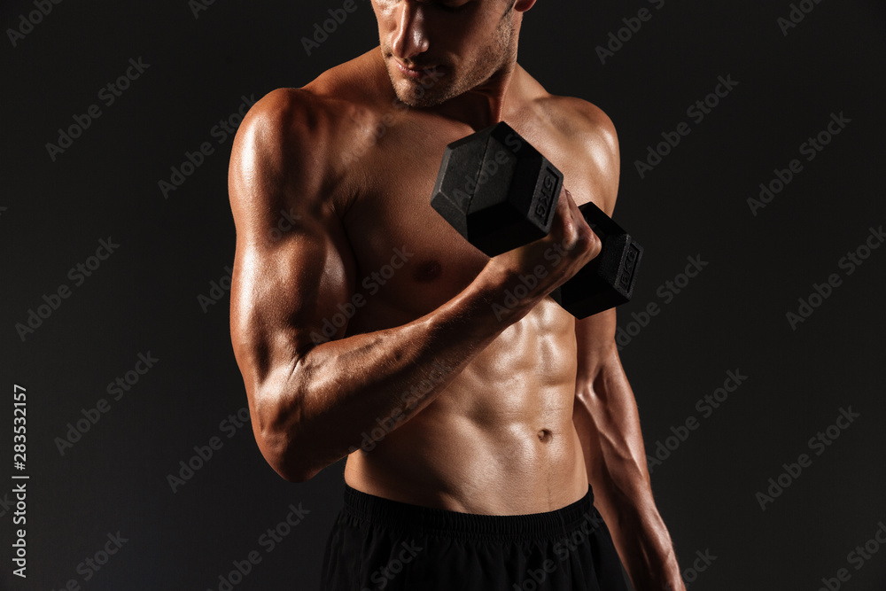 Concentrated handsome young strong sportsman posing isolated over black wall background holding dumbbells.