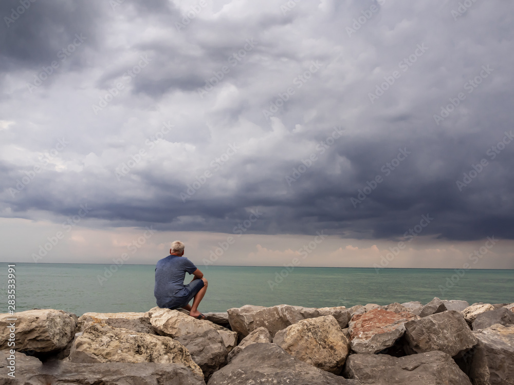 Mann mit Blick aufs Meer auf Felsen stizend, Gewitterwolken, Klimawandel Mann mit Blick aufs Meer auf Felsen stizend, Gewitterwolken, Klimawandel