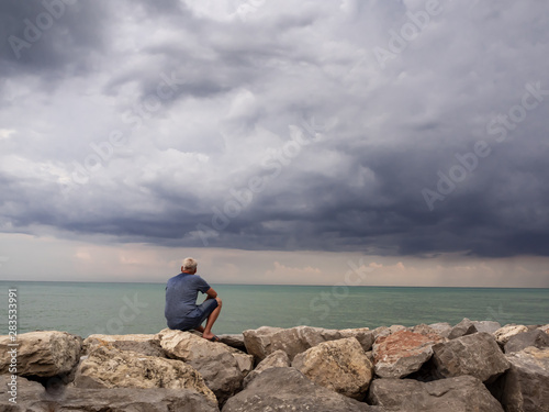 Mann mit Blick aufs Meer auf Felsen stizend, Gewitterwolken, Klimawandel