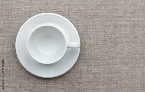 White cup and saucer on natural linen fabric  top view  free space