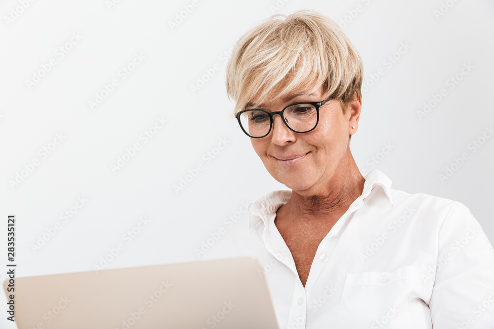 Image closeup of blond adult woman wearing eyeglasses smiling while using laptop computer Image closeup of blond adult woman wearing eyeglasses smiling while using laptop computer