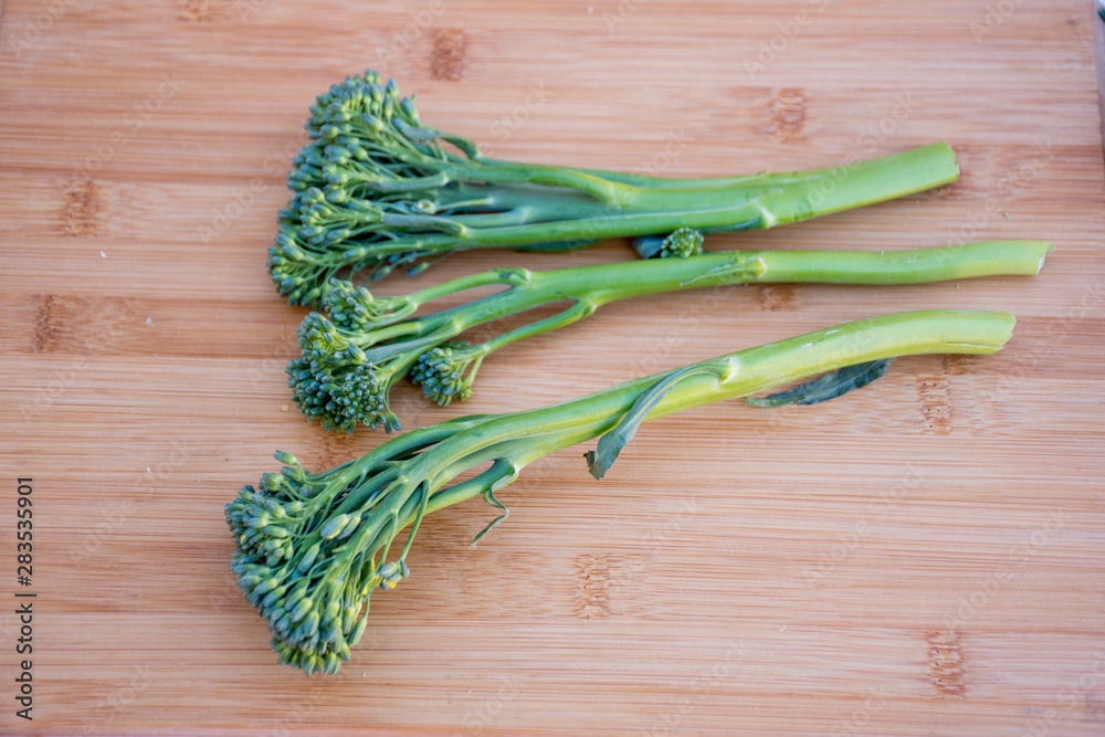 Bunch of fresh broccolini on a wooden board background. Healthy eating. Hybrid of broccoli and chinese broccoli Bunch of fresh broccolini on a wooden board background. Healthy eating. Hybrid of broccoli and chinese broccoli