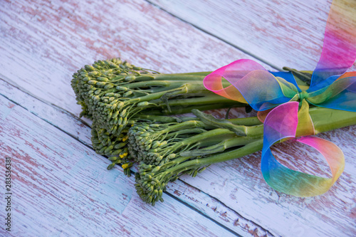 Bunch of fresh broccolini tied with a rainbow ribbon on a wooden table background. Healthy eating. Cooking ingredient photo