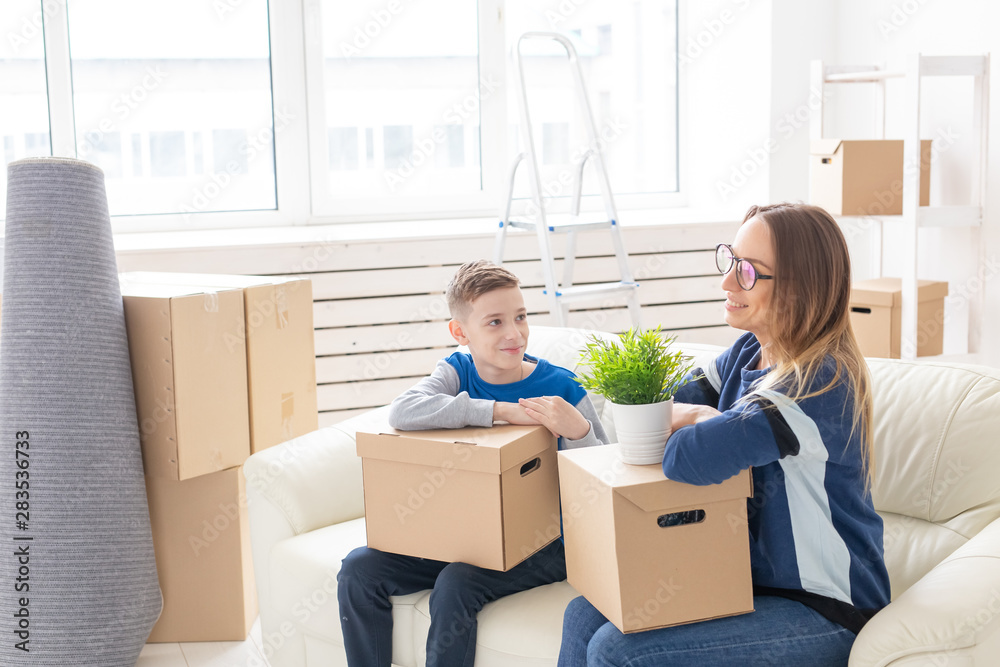 Cute mom and little boy son sort boxes with things after the move. The concept of housewarming mortgage and the joy of new housing.