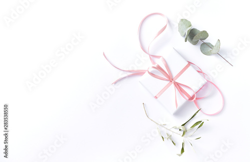White gift box with pink ribbon and dry eucalyptus leaves on white background. Flat lay. Copy space