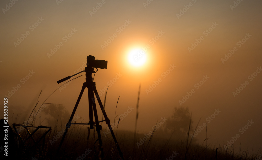 Silhouette of photo camera on sunrise in the fog