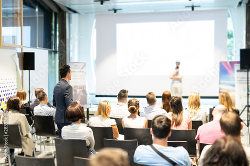 I have a question. Group of business people in conference hall. Businessman in audience standing and asking question to speeker. Conference and Presentation. Business and Entrepreneurship. photo