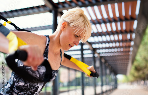 Fotografija A young sportswoman doing exercise with TRX fitness straps outdoors