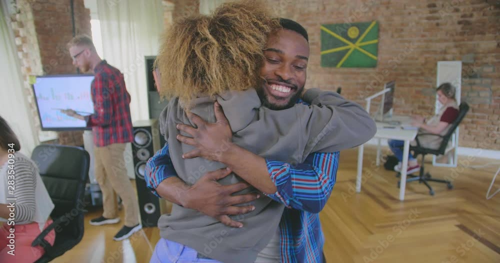 Backside view of young black woman who greets and hugs her smiling male colleague