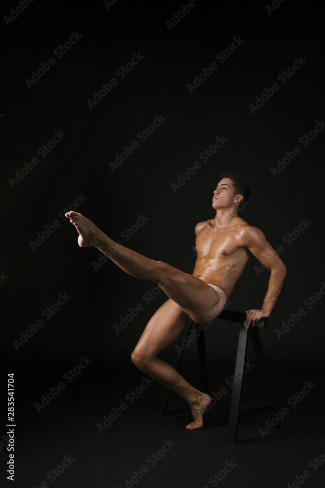 Shirtless dancer lifting leg near barre