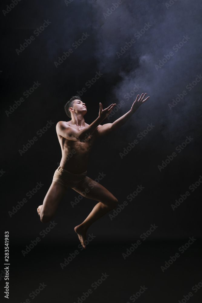 Naked man jumping and raising hands against black background