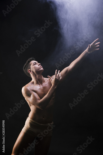 Naked athletic man standing and raising hands near smoke © Freepik