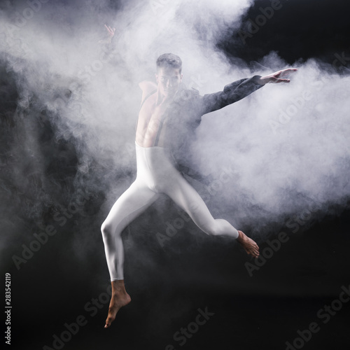 Young athletic man jumping and dancing near smoke