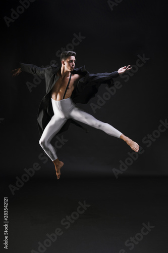 Young man in stylish clothes jumping and dancing on black background