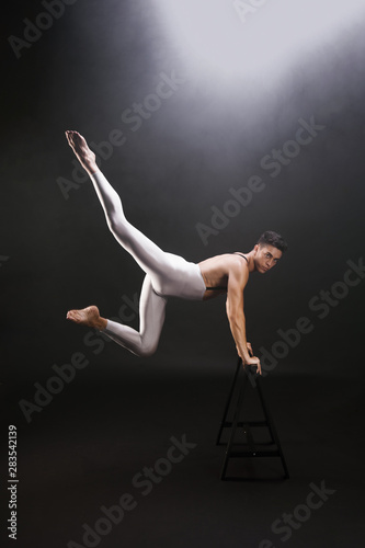 Young man with naked torso jumping and leaning on wooden stand while looking at camera