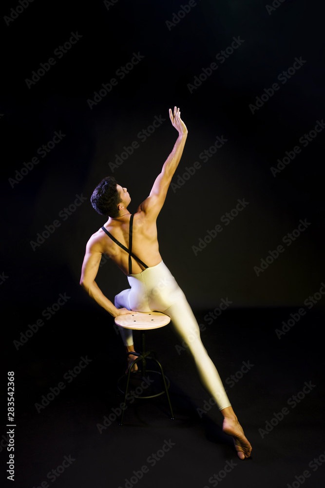 Graceful male ballet dancer stretching in spotlight
