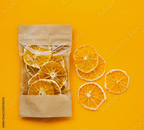 Healthy snack. Fruit chips from organic oranges in a paper bag on a bright orange background and a few circles of chips nearby.