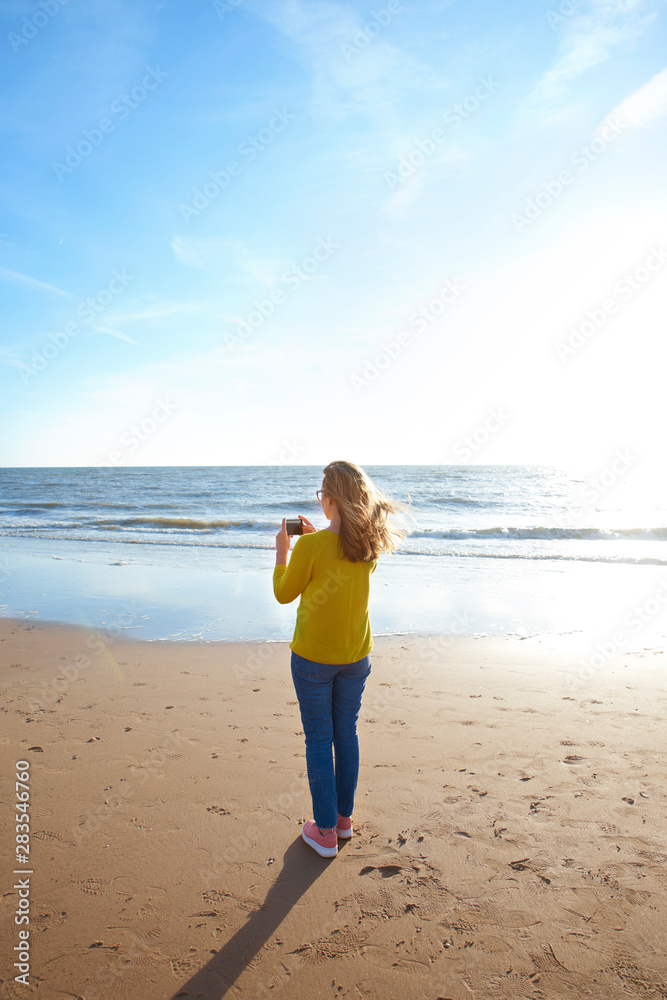 Woman standing on the beach and and take a picture of the sea