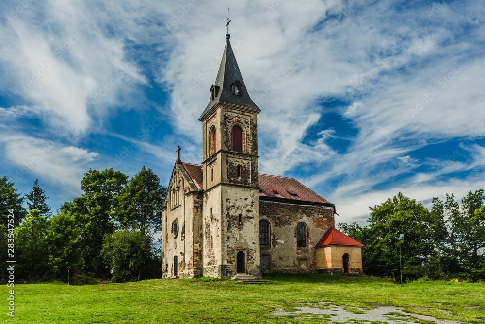 Krasikov, Kokasice / Czech Republic - August 9 2019: View of the old church of Mary Magdalene. Bright sunny summer day with blue sky and white clouds, green grass and trees.