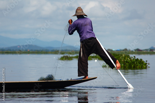 Traditional fisherman working with his net while steering his old boat with only one leg on Lake Inle, Myanmar/Birma.