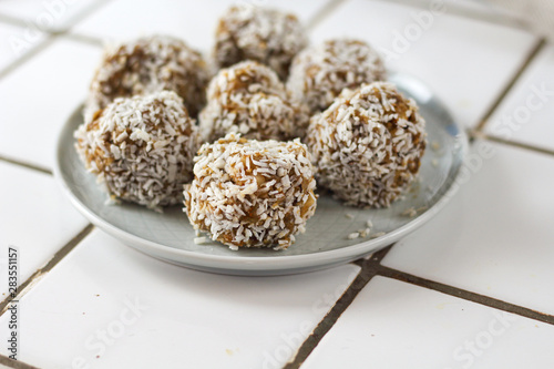 vegetarian raw healthy diet  no bake candies balls dessert sweets sugar free gluten-free with coconut flakes, proper nutrition snack on blue plate on a white tile background, soft selective focus