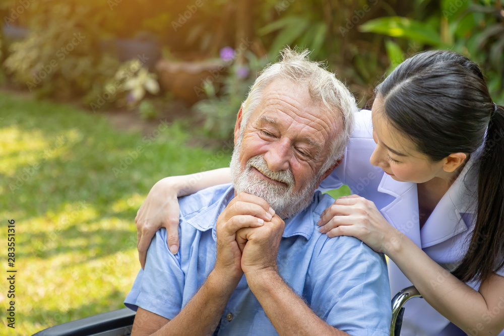Nurse take care and comfort elderly man on wheelchair in garden at nursing home Nurse take care and comfort elderly man on wheelchair in garden at nursing home