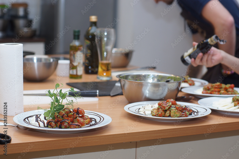 A cook in an apron sets the table for several people, laying out tomatoes in a caprese salad with pesto A cook in an apron sets the table for several people, laying out tomatoes in a caprese salad with pesto