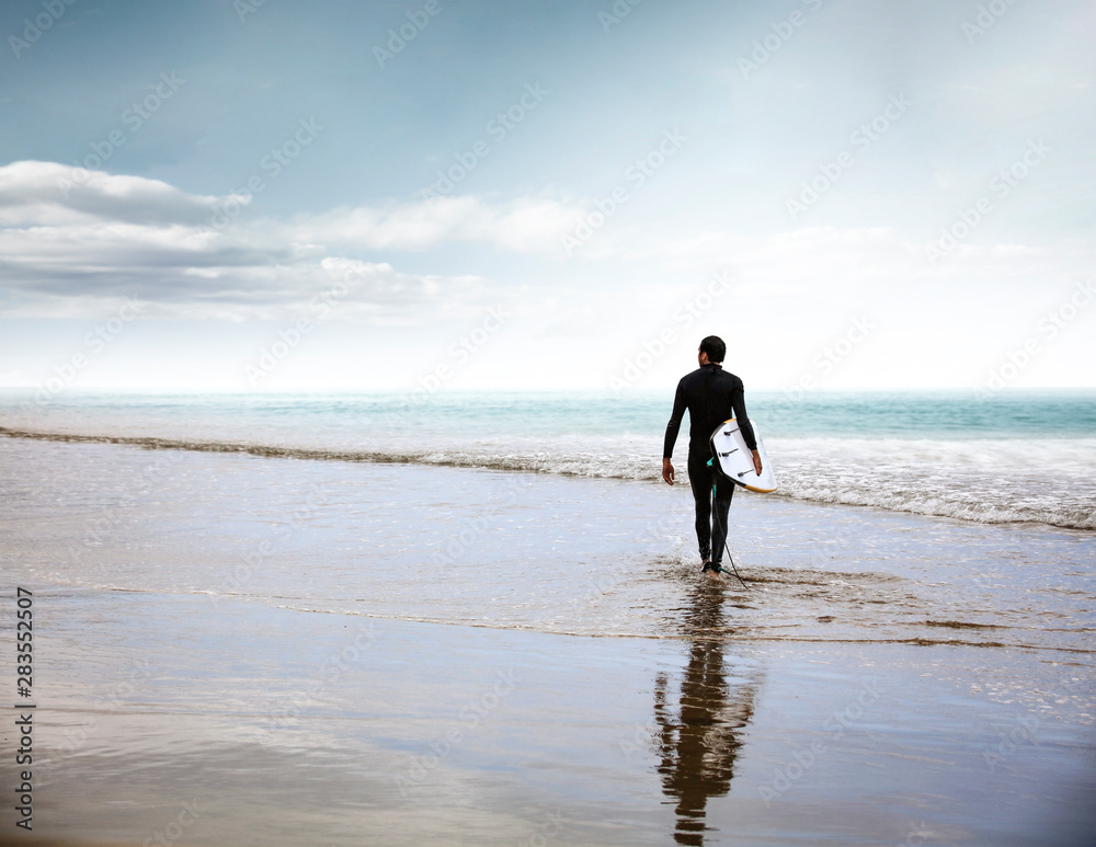 Surfer on the beach and sandy wavy sea shore in the late afternoon Surfer on the beach and sandy wavy sea shore in the late afternoon