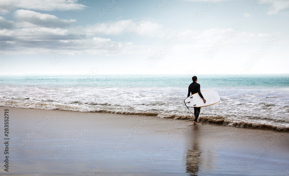 Surfer on the beach and sandy wavy sea shore in the late afternoon Surfer on the beach and sandy wavy sea shore in the late afternoon