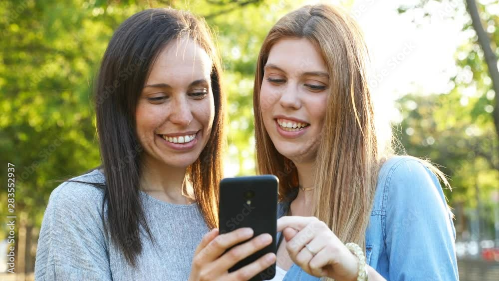 Happy adult woman and teenage girl checking smart phone in a park Happy adult woman and teenage girl checking smart phone in a park