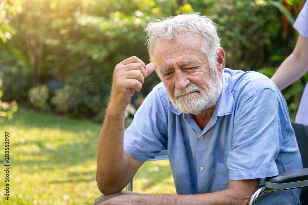 Depressed thoughtful elderly man on wheelchair with nurse in garden at nursing home Depressed thoughtful elderly man on wheelchair with nurse in garden at nursing home