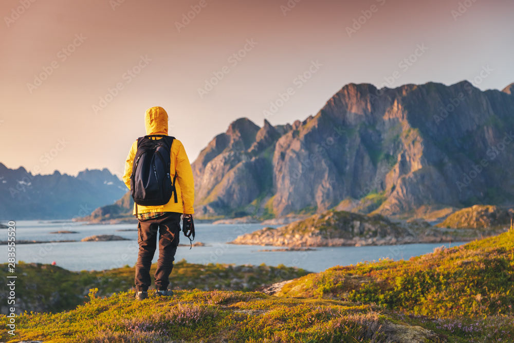 Φωτογραφία A traveler in a yellow jacket looks at the sunset on the Lofoten Islands, travel