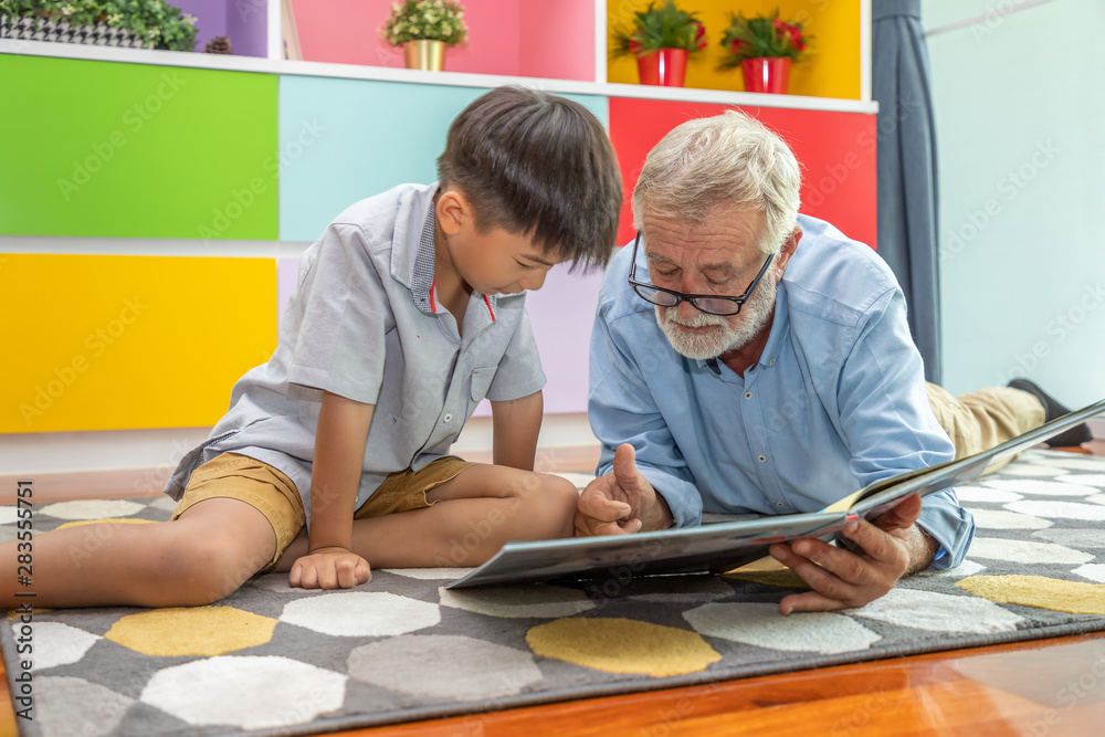 Happy boy grandson reading book with old senior man grandfather at home Happy boy grandson reading book with old senior man grandfather at home