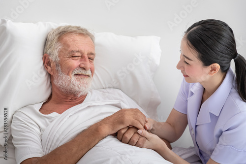 Happy nurse holding elderly man hands with blanket in bedroom at nursing home