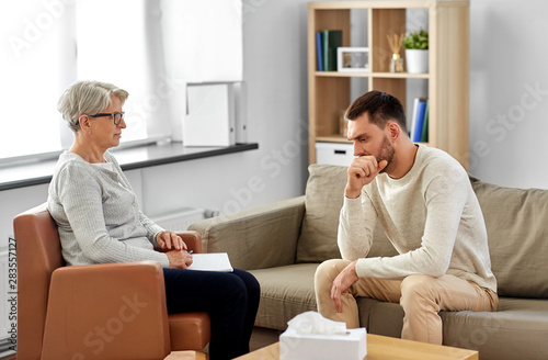 psychology, mental therapy and problem concept - senior woman psychologist taking notes to notebook and sad young man patient at psychotherapy session © Syda Productions