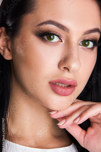 Close-up portrait of sensuality young brunette girl with green eyes  woman with stylish make up is looking straight and posing cute with hand near her face  beauty concept
