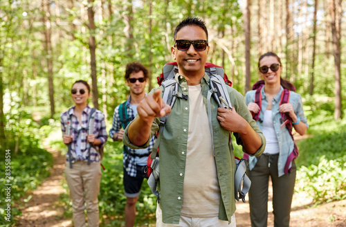 travel, tourism, hike and people concept - group of friends with backpacks and indian man pointing finger to you in forest © Syda Productions